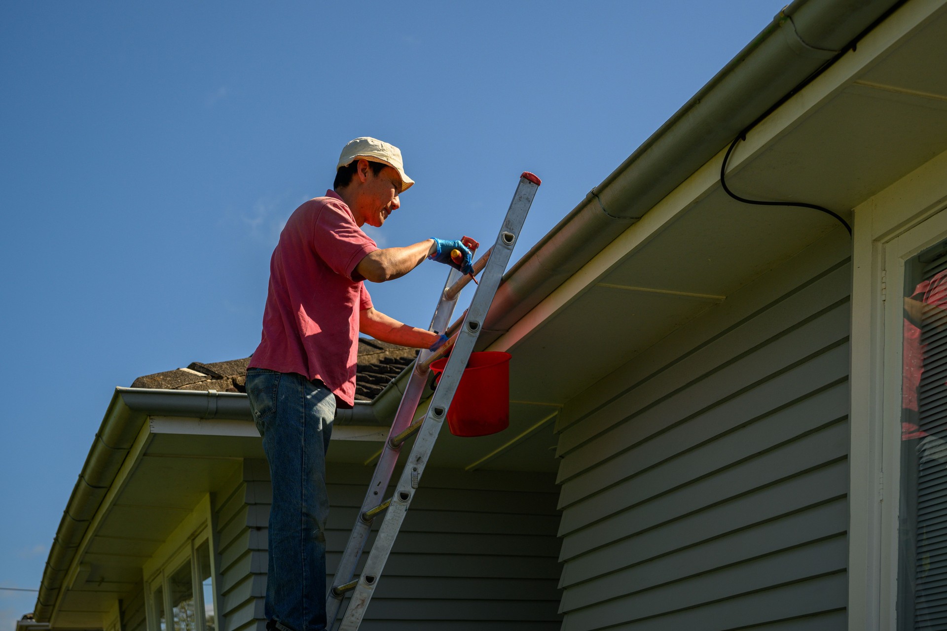 Man standing on the ladder and cleaning the gutter. Home maintenance work. Auckland.