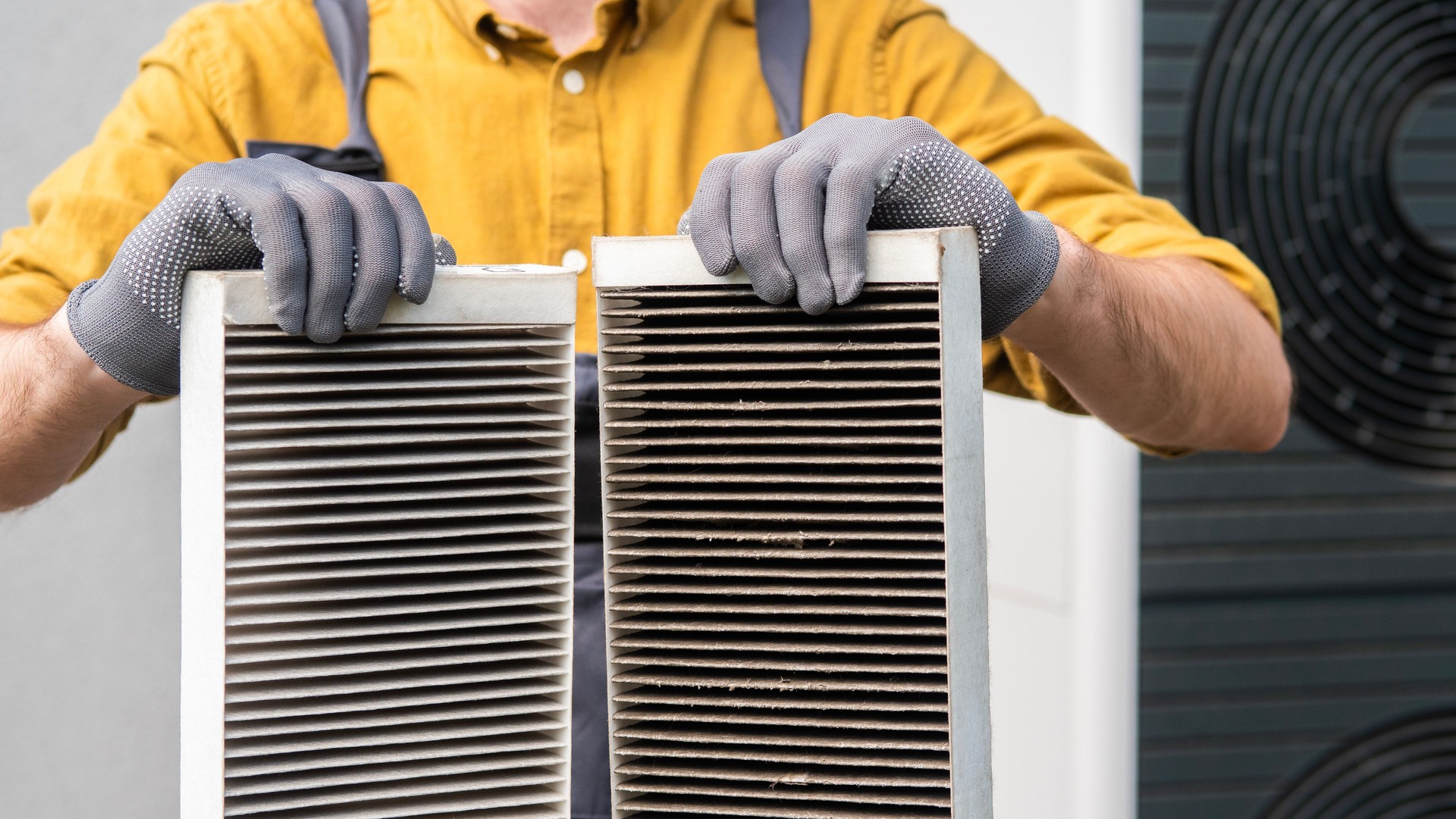 Worker holding two dirty air filters from a home ventilation system.